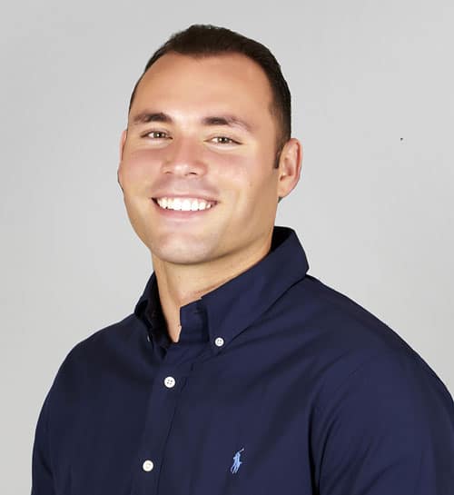 Headshot of a man smiling, wearing a navy blue shirt, in front of a white background